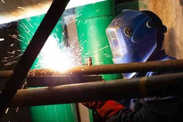 A man wearing a welding mask is welding a pipe.