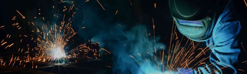 A man wearing a welding mask is welding a piece of metal.