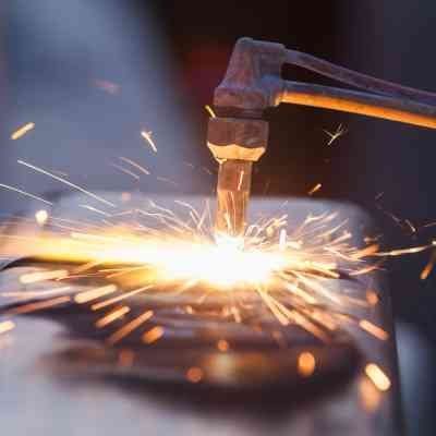 A close up of a torch cutting a piece of metal with sparks coming out of it.