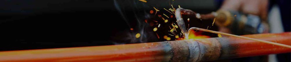 A close up of a person welding a pipe with sparks coming out of it.