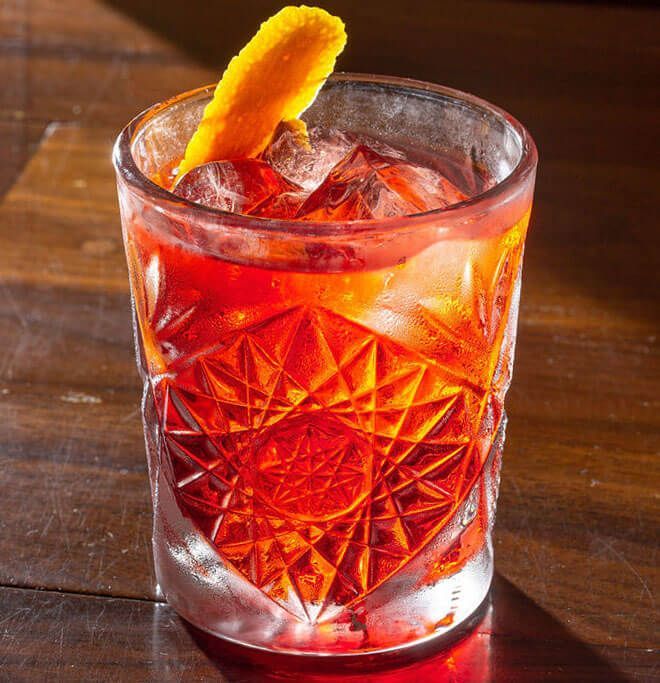 A glass of red liquid with ice and an orange peel
