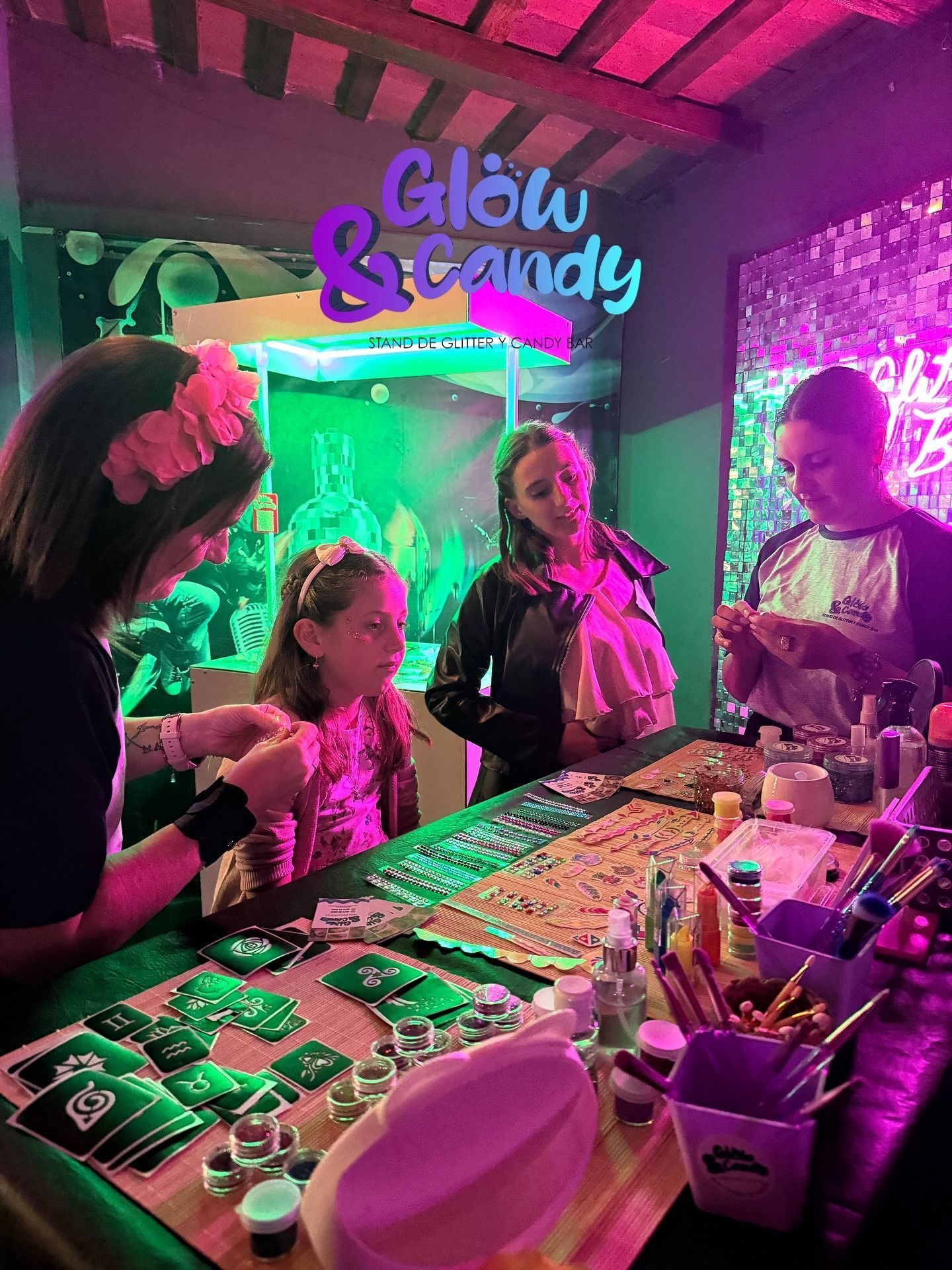 En una feria, un puesto de Glow & Candy con personal sirviendo dulces coloridos bajo luces rosas y verdes.