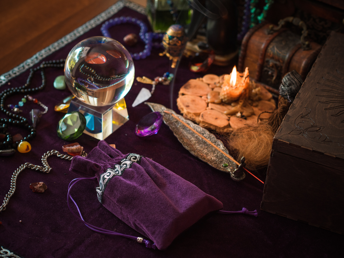 Crystal ball, candle, purple velvet pouch, and assorted crystals arranged on a dark purple cloth surface.