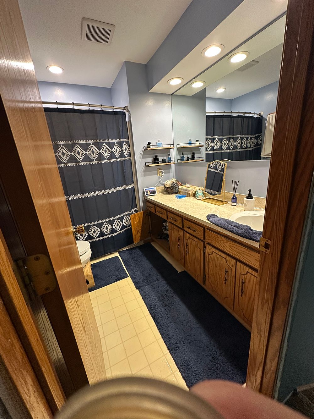 Bathroom with blue walls, wood vanity, mirror, shower curtain, and a blue rug.