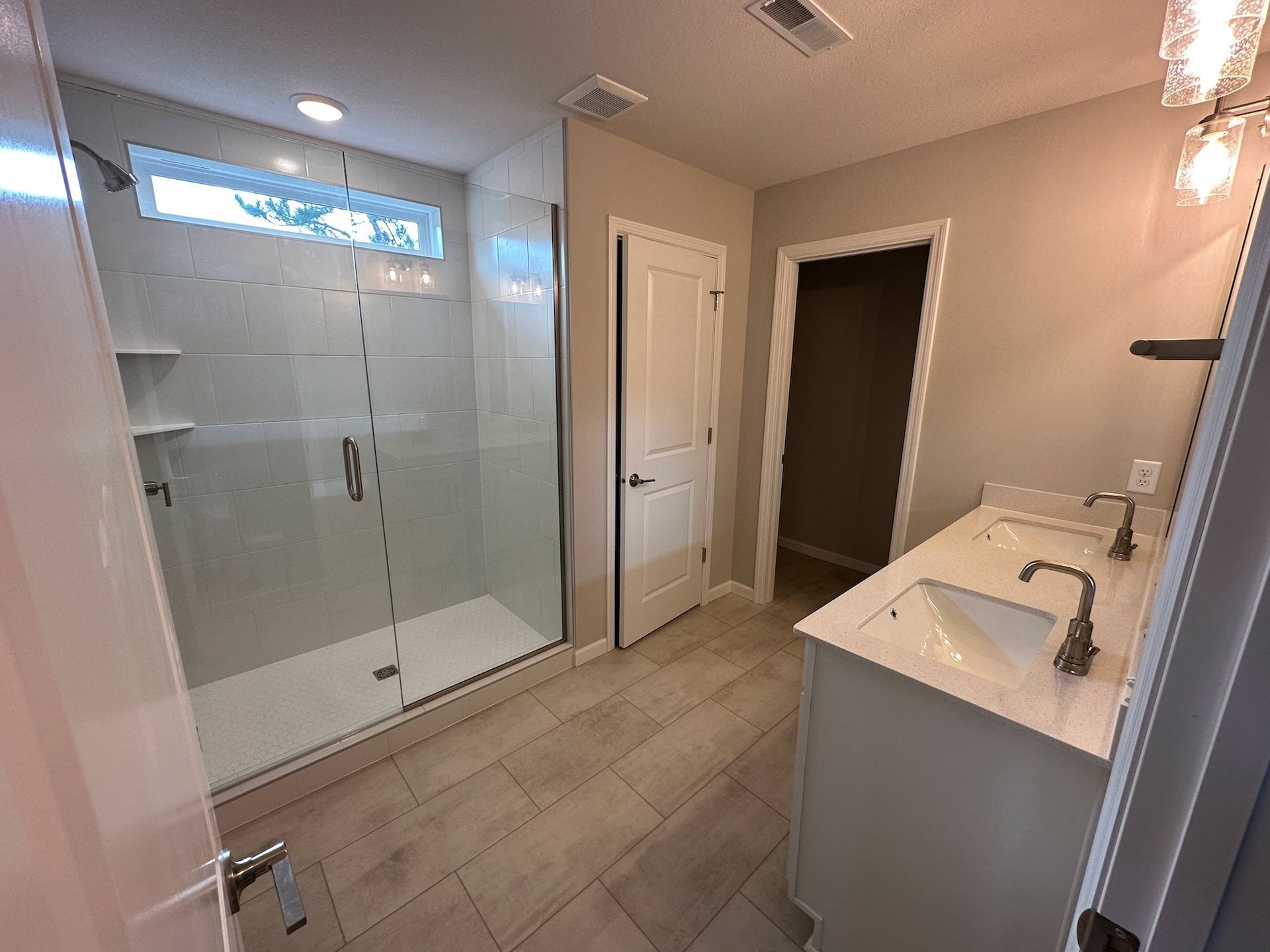 Modern bathroom with a glass shower, double vanity, and beige tile flooring.