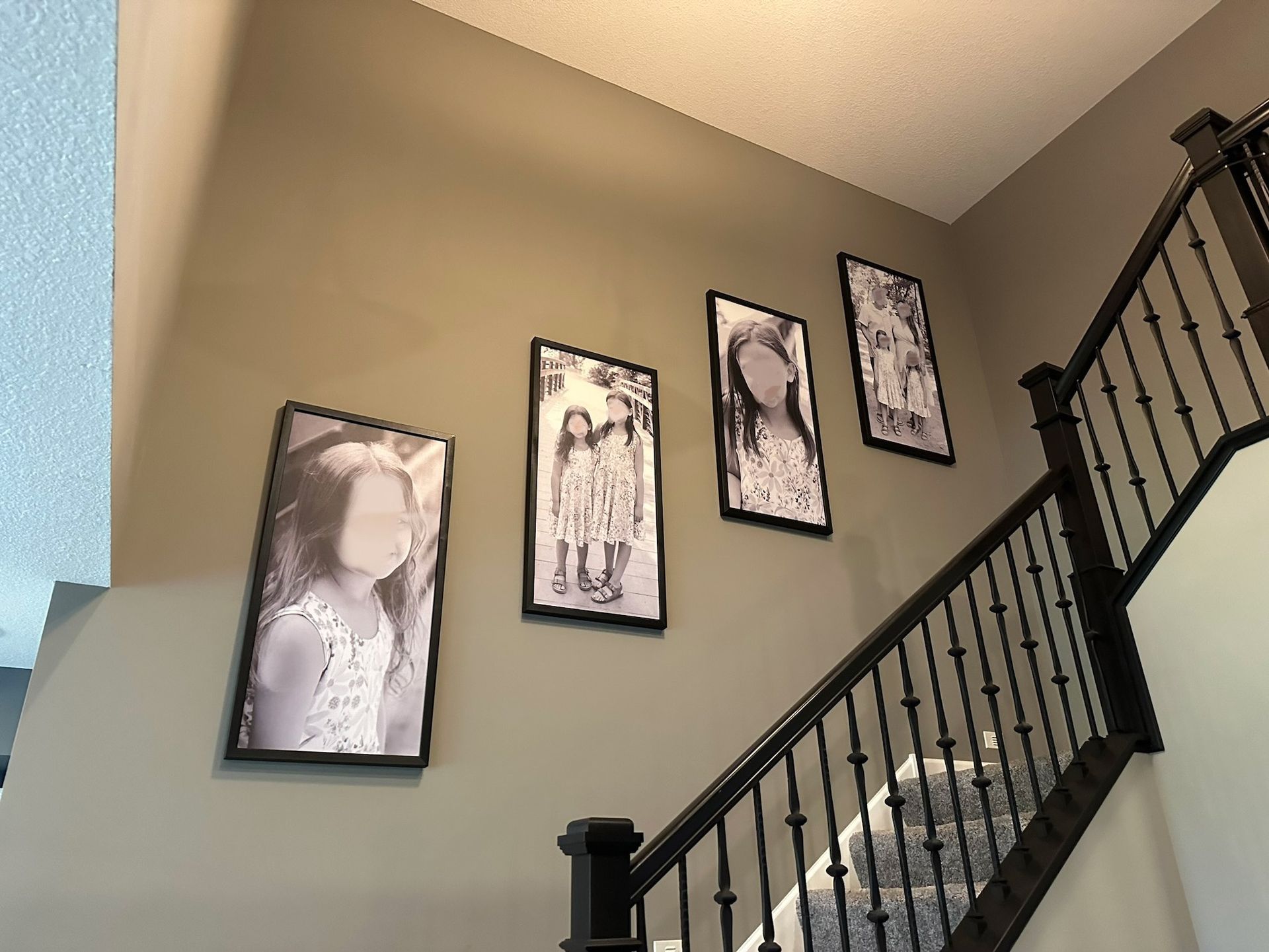 Four framed photos on a gray wall above a staircase with a black railing.