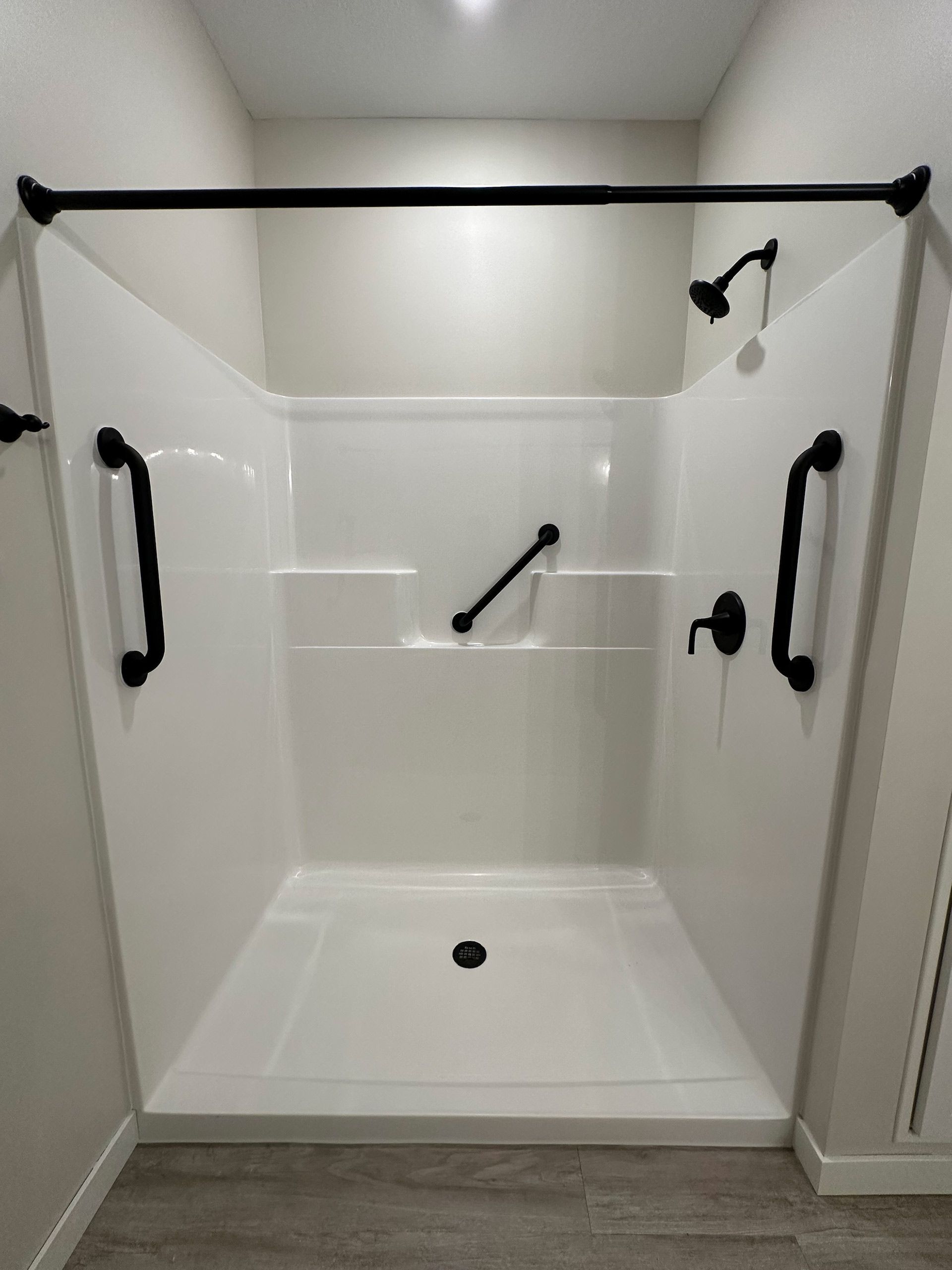 White accessible shower with black grab bars, fixtures, and curtain rod.