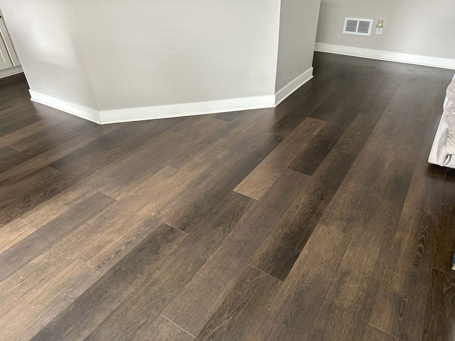 Dark wood-look flooring extends across a room with white baseboards and a gray wall.