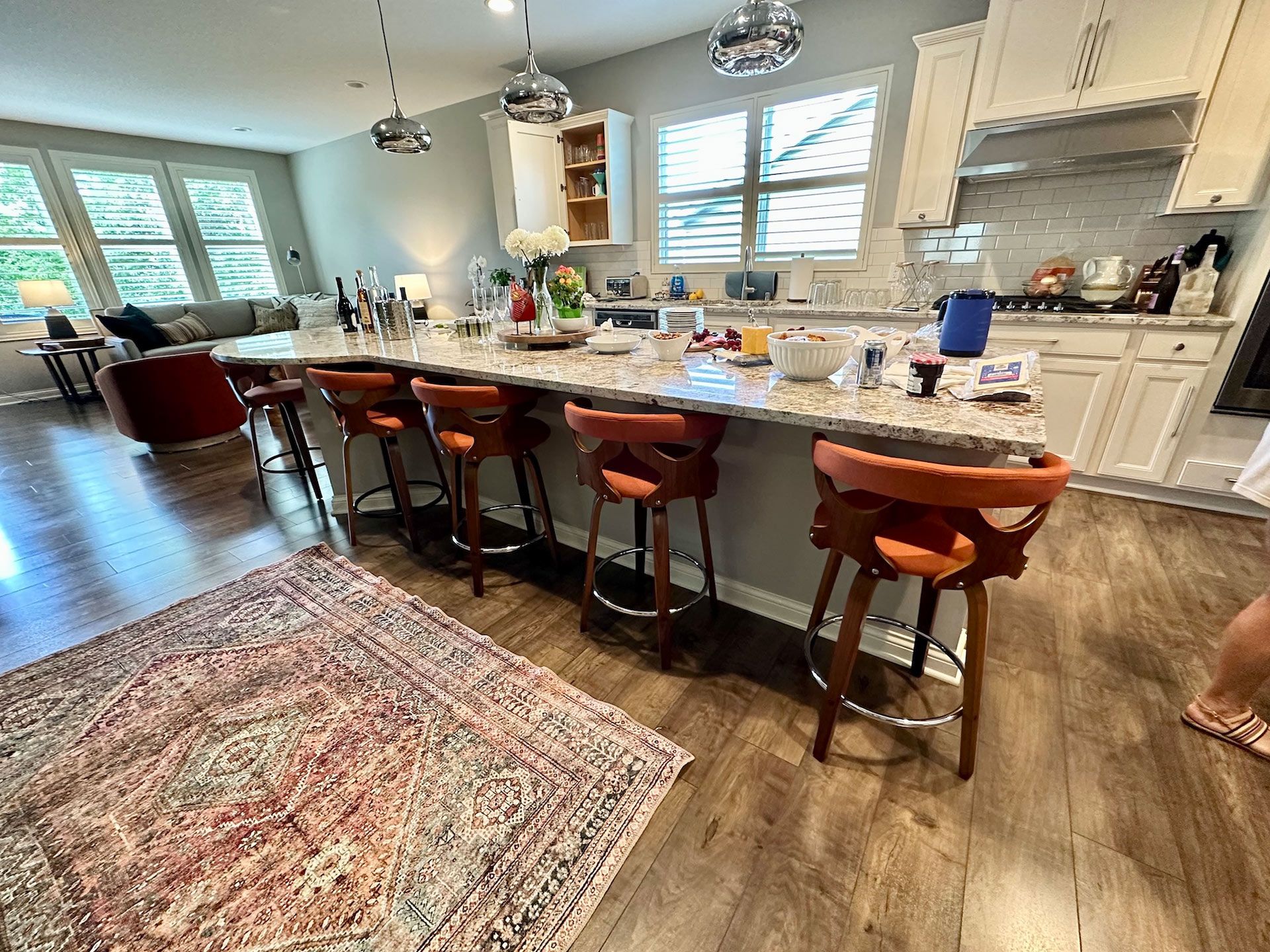 Kitchen with island and brown leather bar stools, rug, and windows.