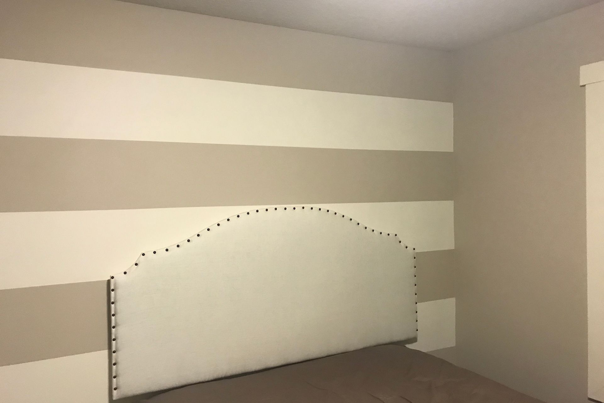 Bedroom with beige and white striped wall behind a bed with a white headboard.