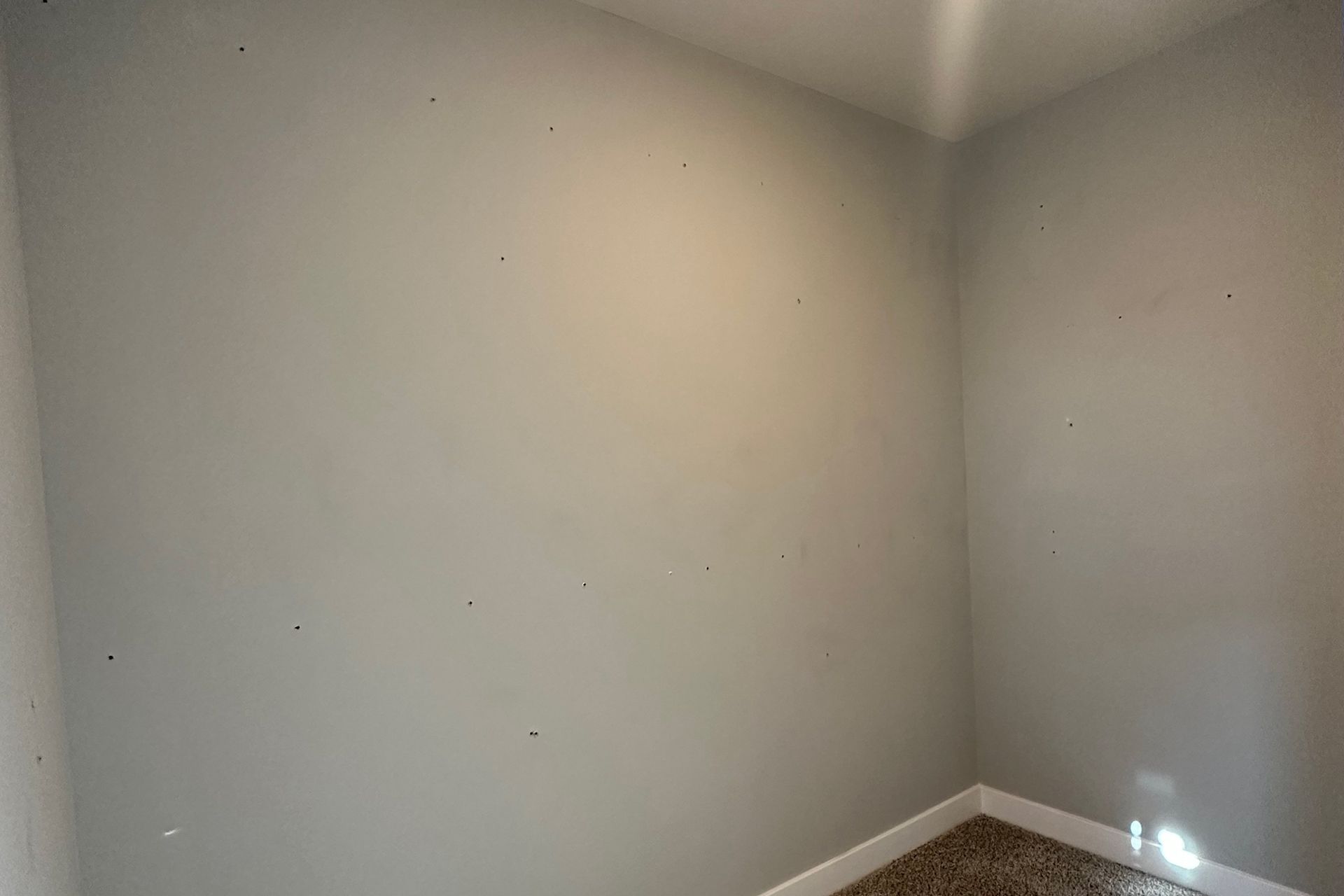 Empty room with gray walls, a corner, and carpeted floor.