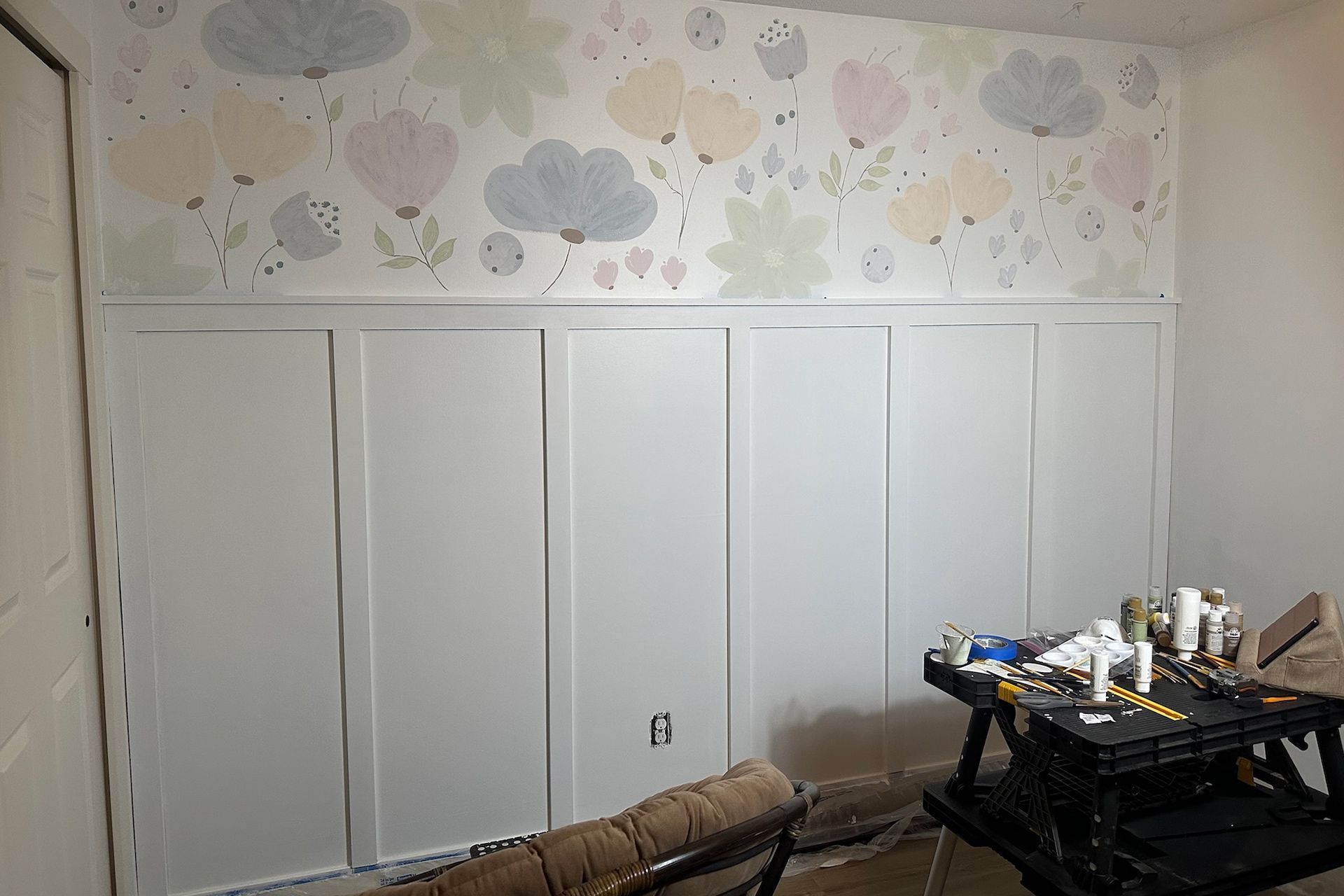 White paneled wall below floral wallpaper in a room with a work table.