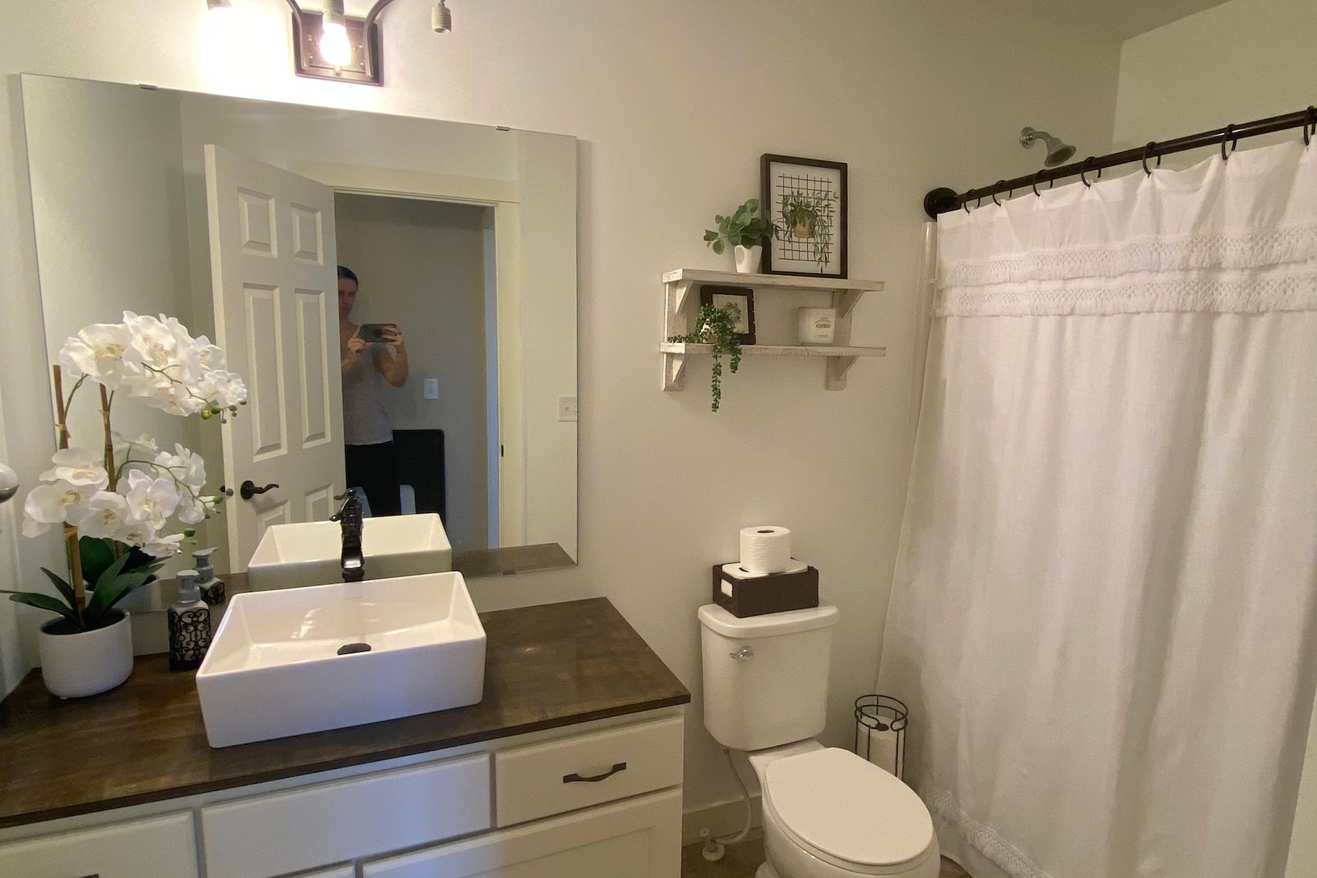 Bathroom with white sink, toilet, and shower, light gray walls, and decorative plants.