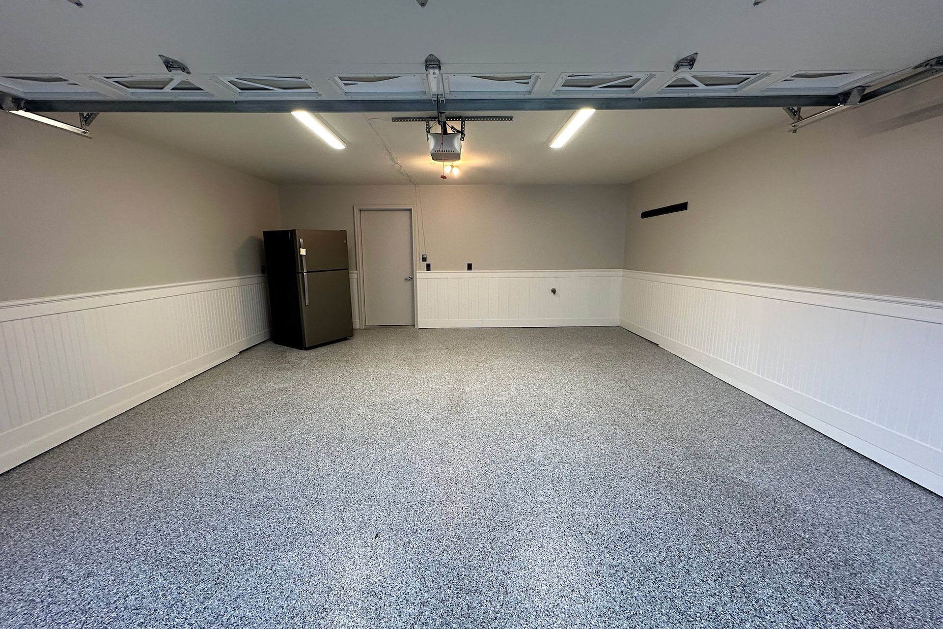 Empty garage with epoxy floor, white walls, and a black refrigerator.