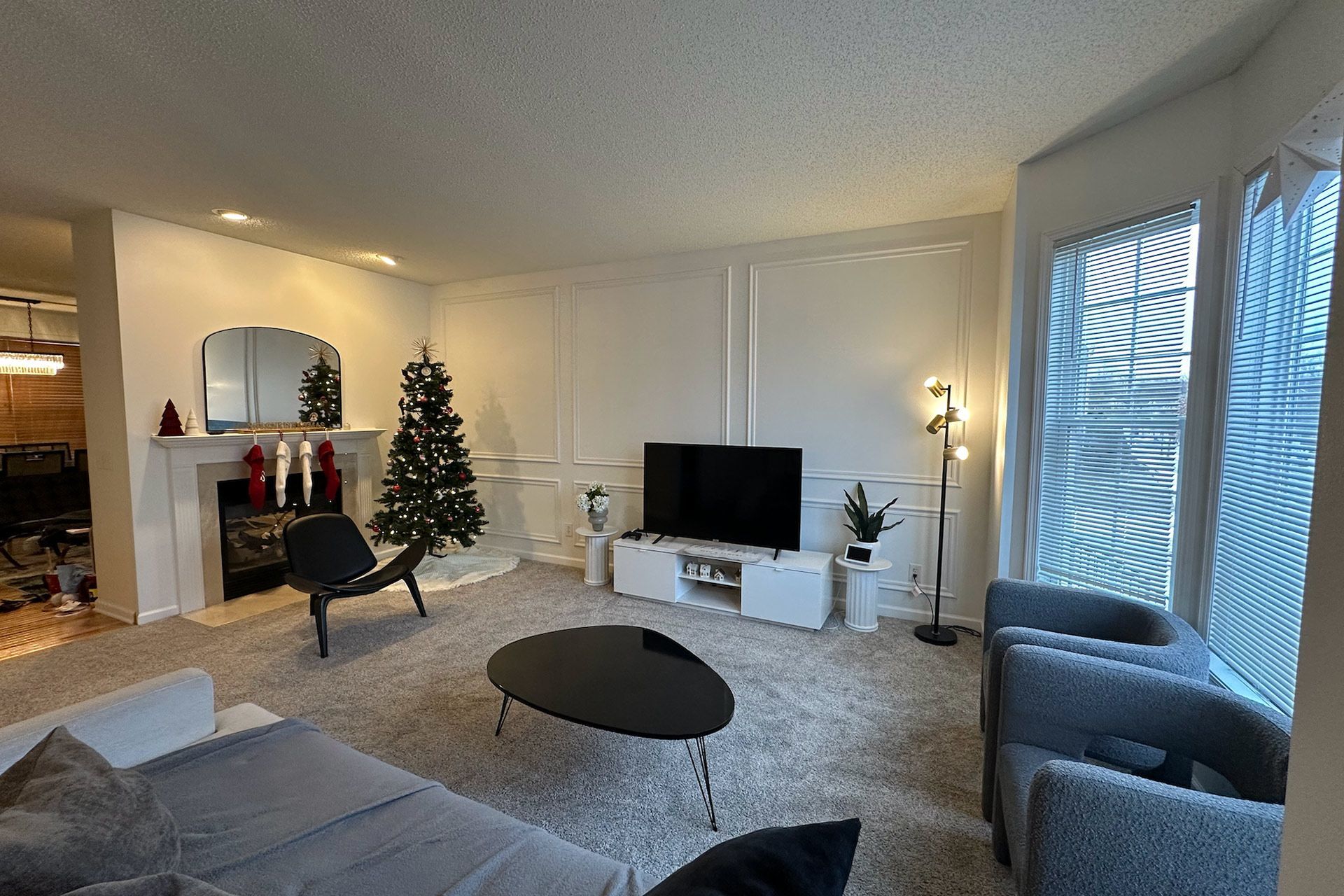 Living room with Christmas tree, fireplace, TV, and modern furniture; white walls, neutral carpet.
