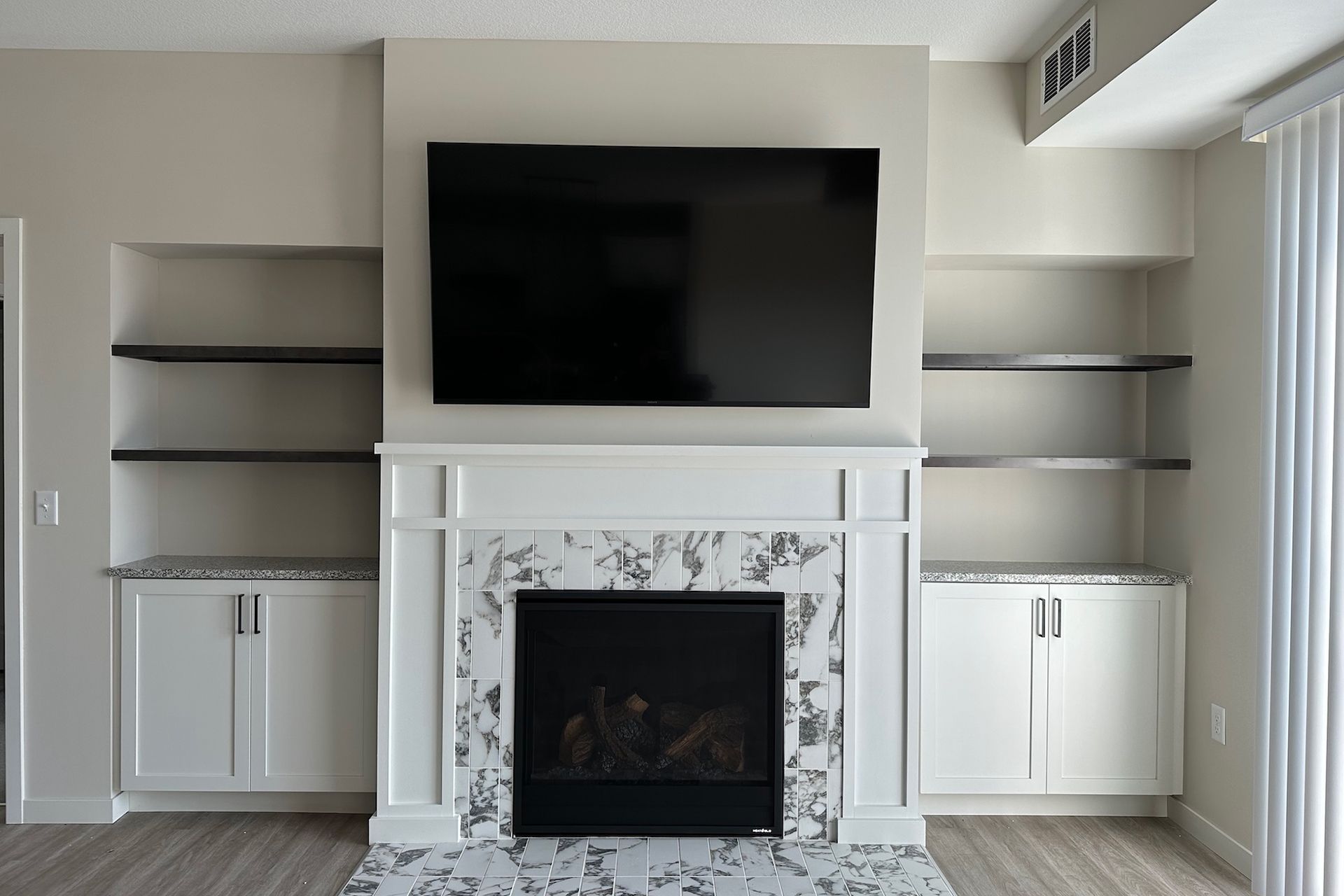 Living room with fireplace, built-in shelves, cabinets, and a mounted television.