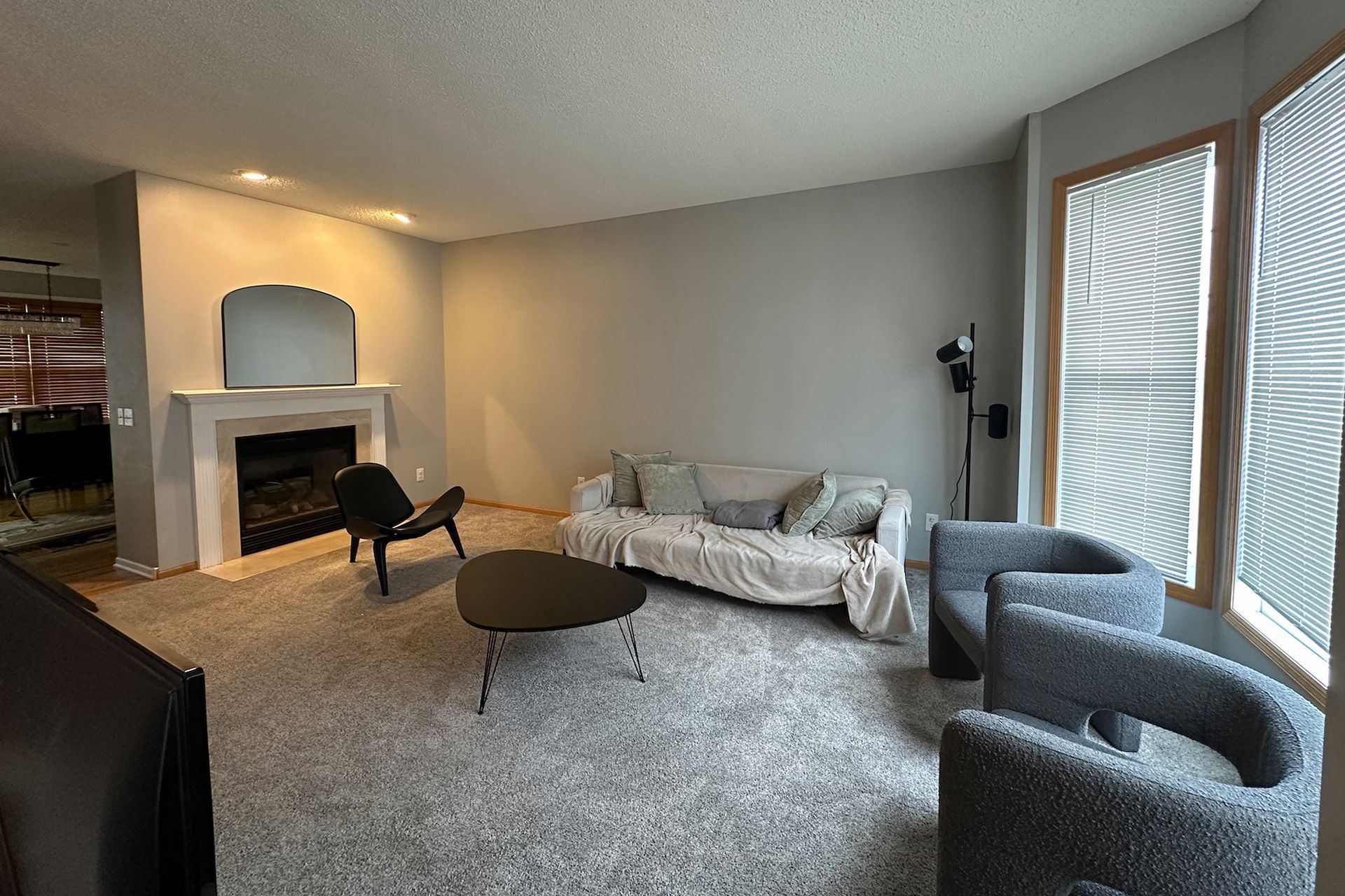 Living room with gray walls, fireplace, sofa, chairs, coffee table, and window with blinds.