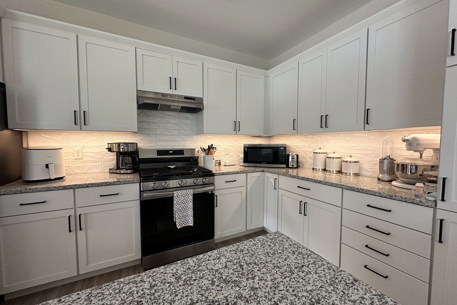 White kitchen with granite countertops, appliances, and cabinetry.