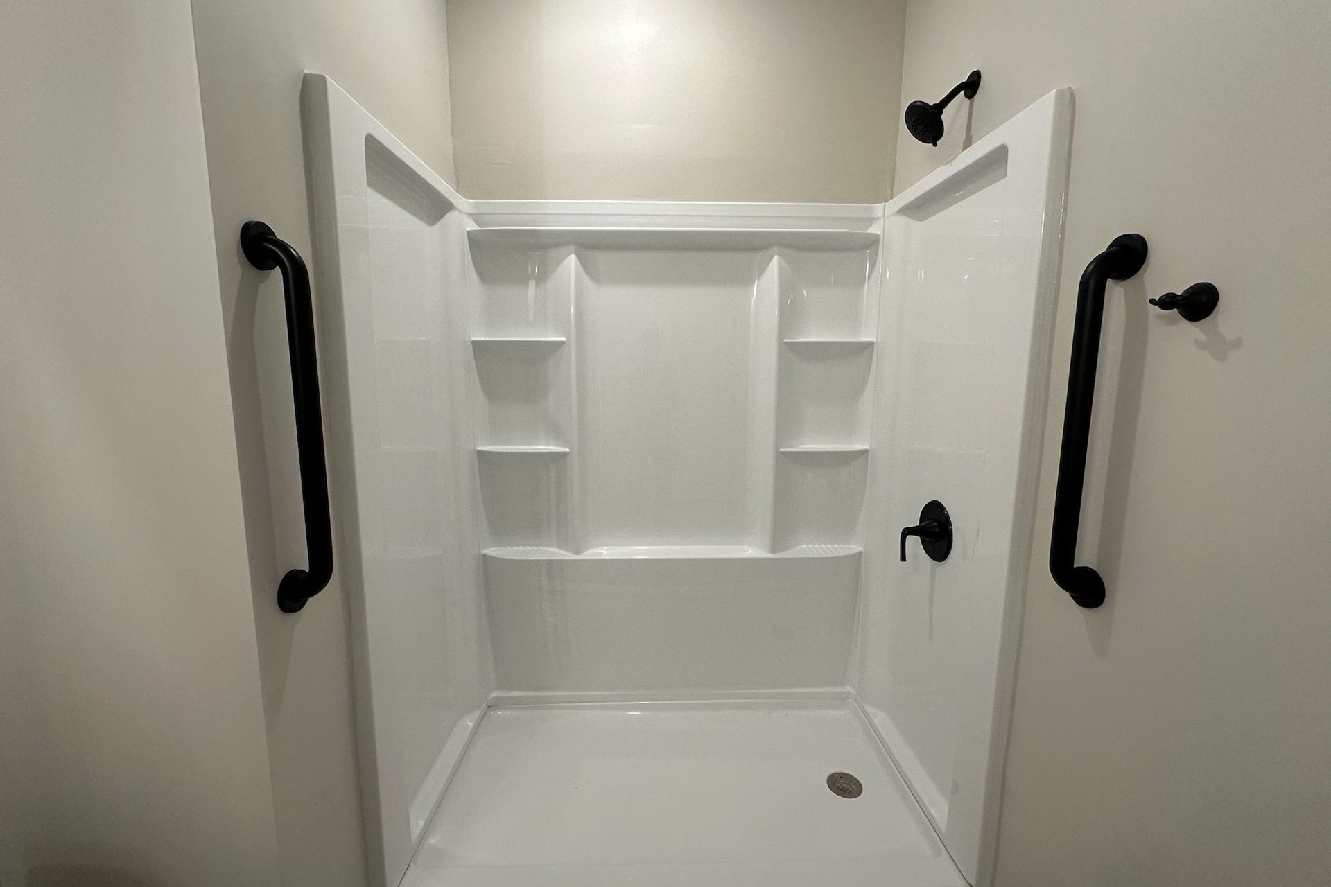 White handicap-accessible shower with black grab bars and fixtures.