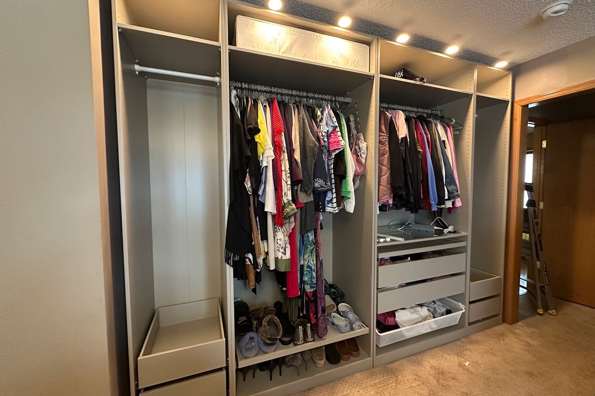 Built-in closet with hanging clothes, drawers, and shoe storage. Beige and gray colors, well-lit.