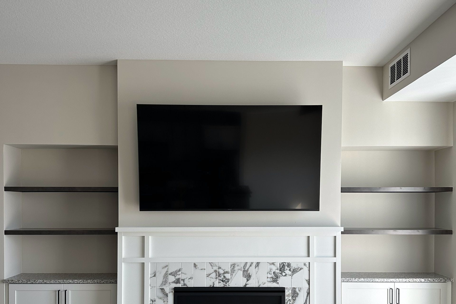 Flat-screen TV mounted above white fireplace with built-in shelves on a light beige wall.
