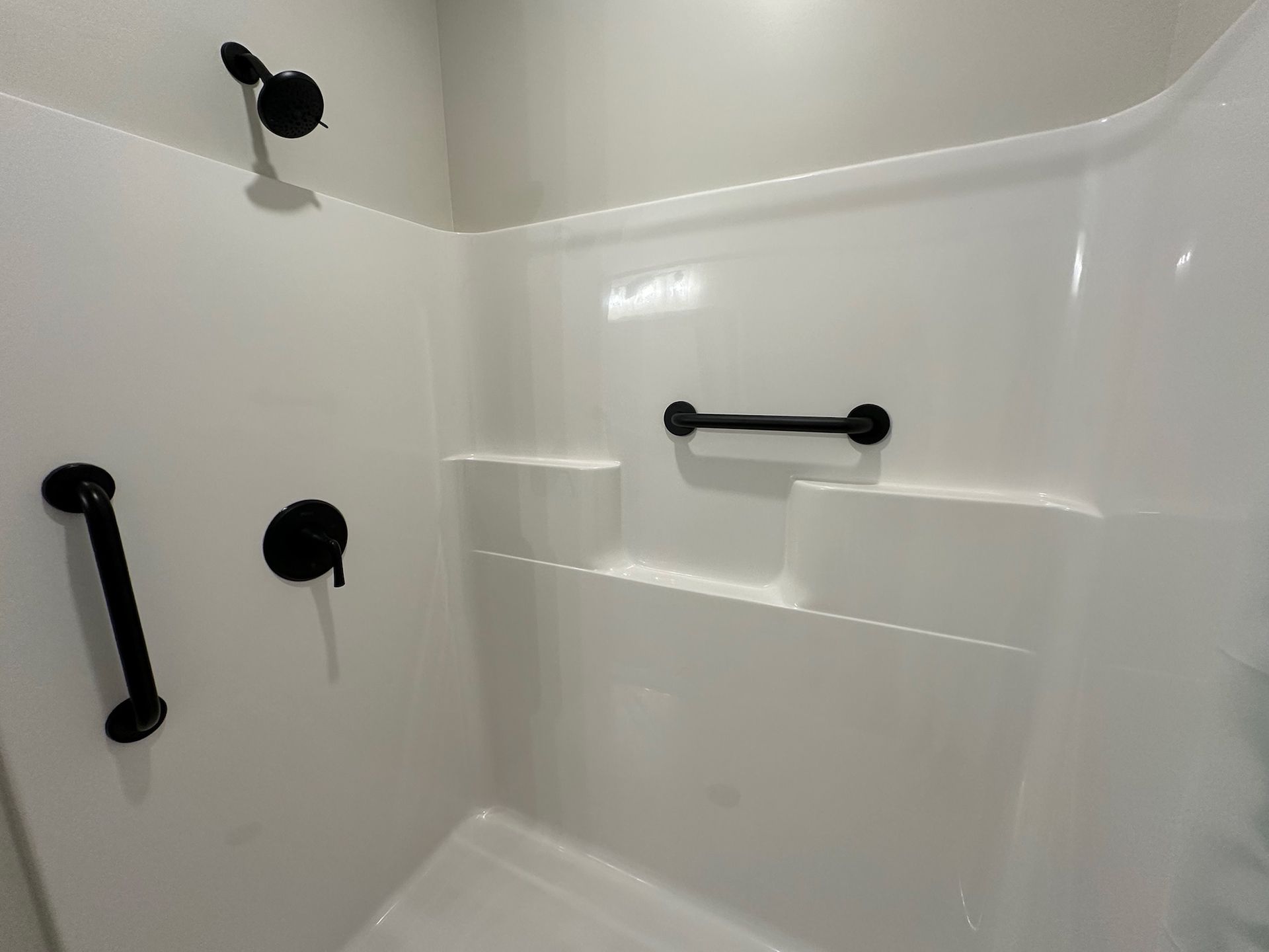 White shower stall with black fixtures and grab bars.