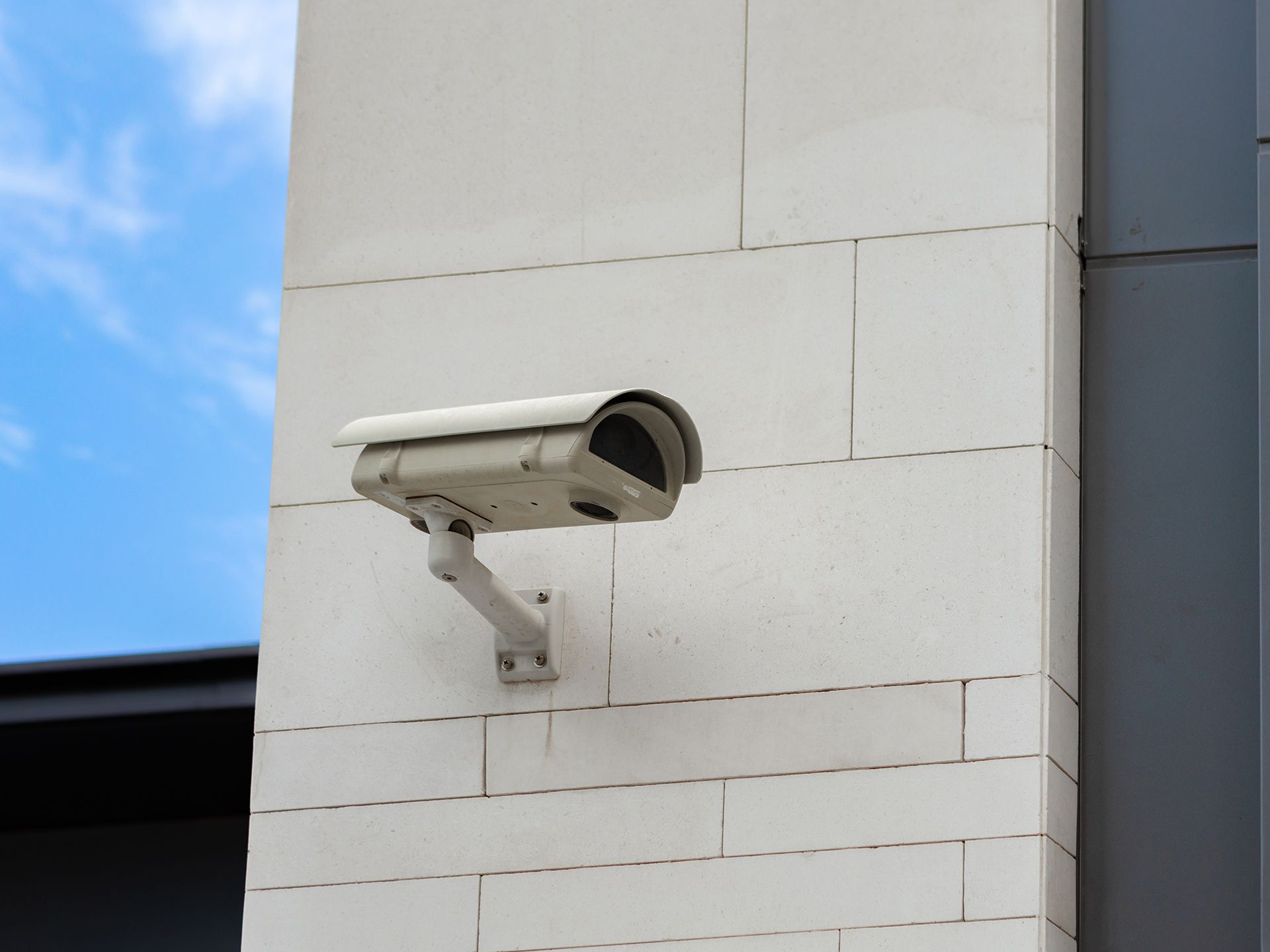 Security camera mounted on a white stone wall, with a blue sky background.