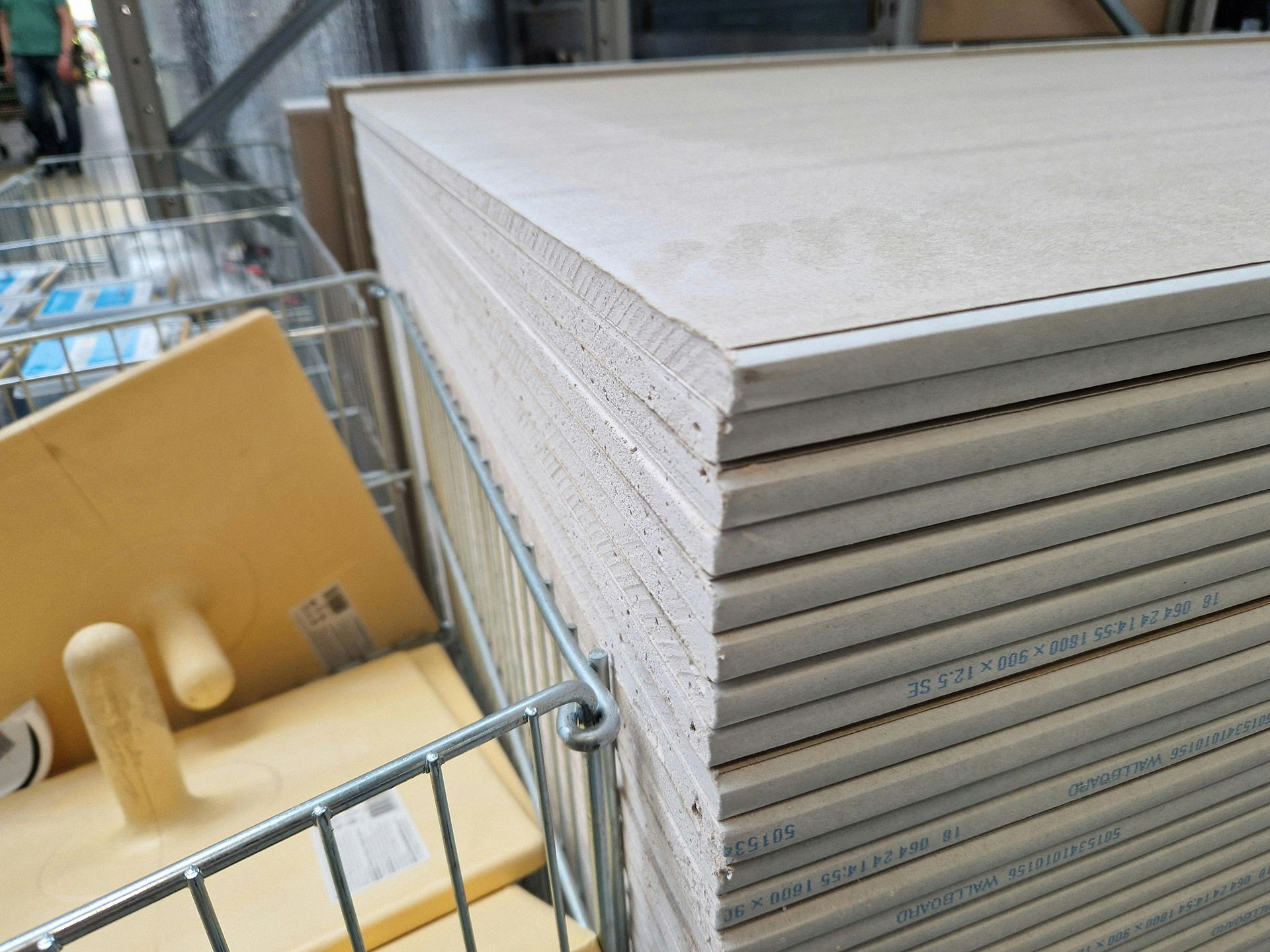 Stack of drywall sheets in a metal shopping cart, construction supply store.
