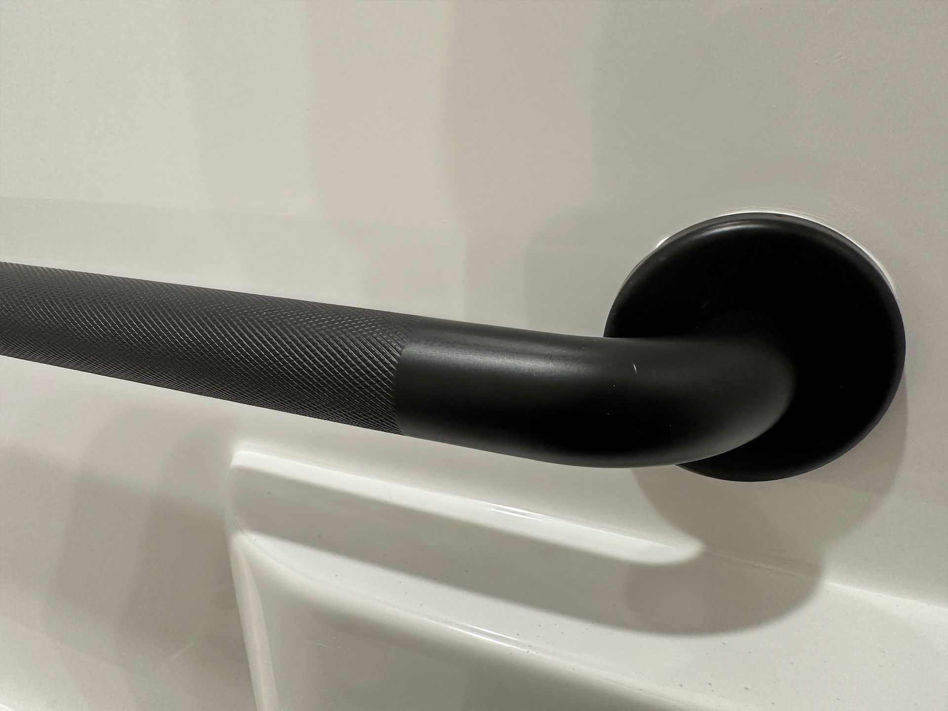 Black textured grab bar mounted on a white wall in a bathroom.
