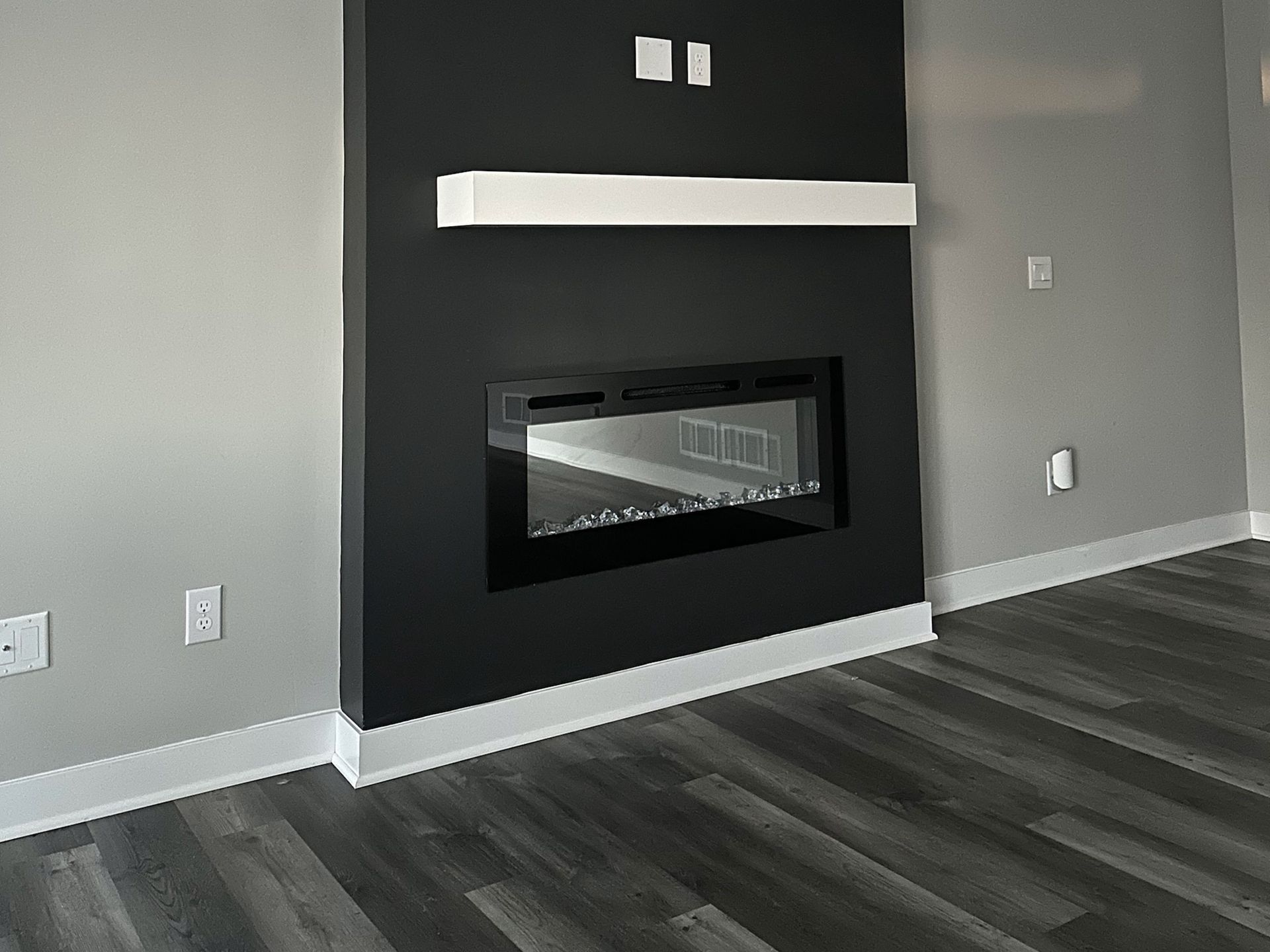 Black fireplace built into a gray wall with a white mantle. Dark wood flooring.