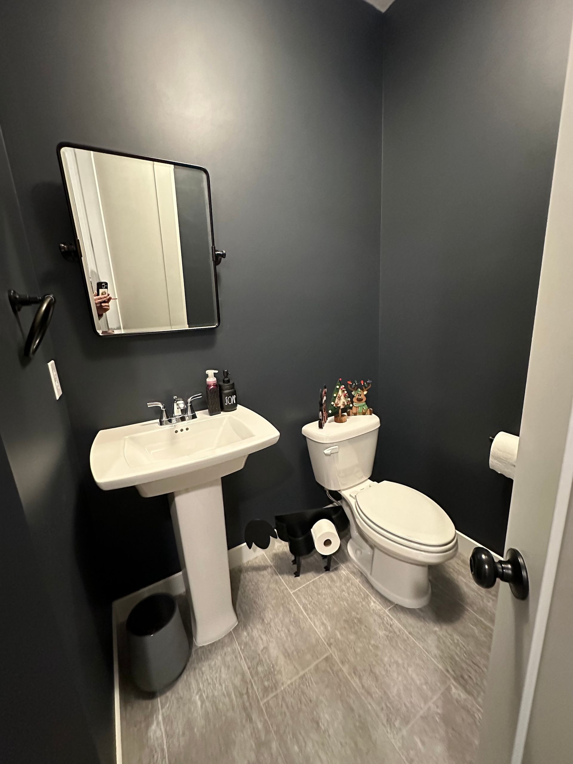 A small, dark gray bathroom with a pedestal sink, toilet, mirror, and gray flooring.