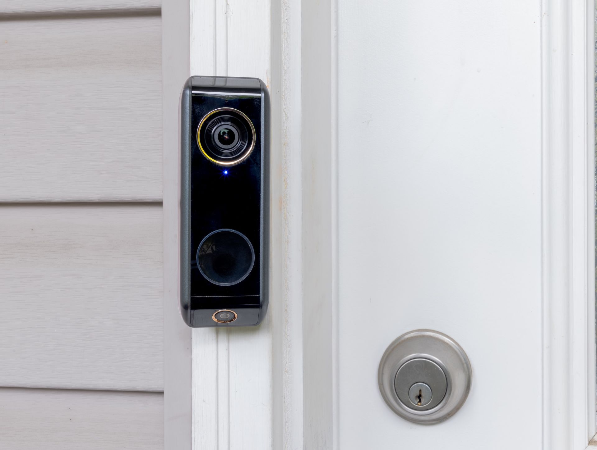 Black video doorbell next to a white door and a gray exterior wall.