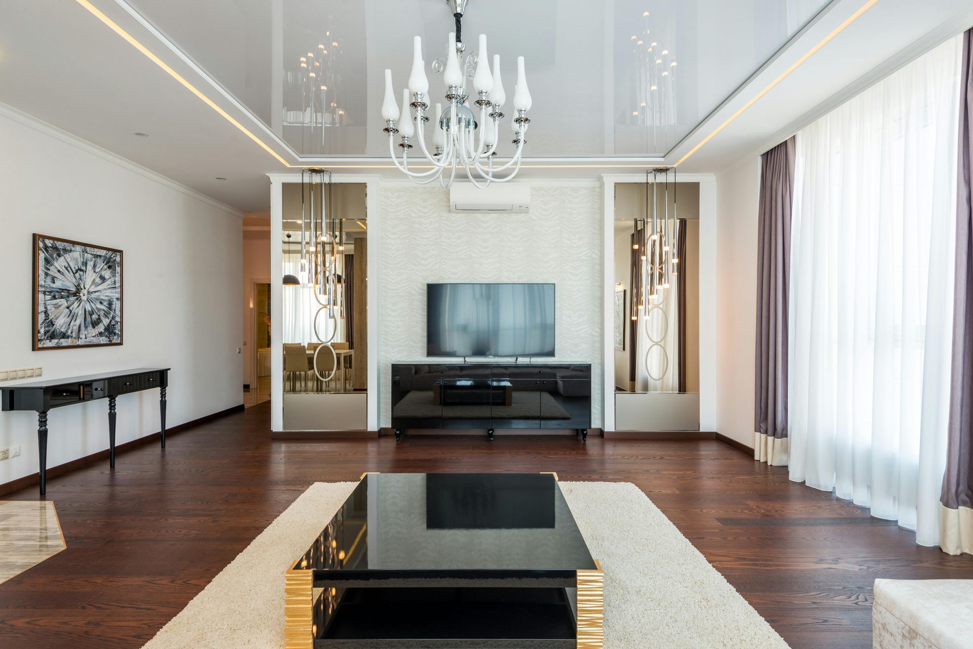 Elegant living room with a modern chandelier, dark wood floors, and a sleek black coffee table. 