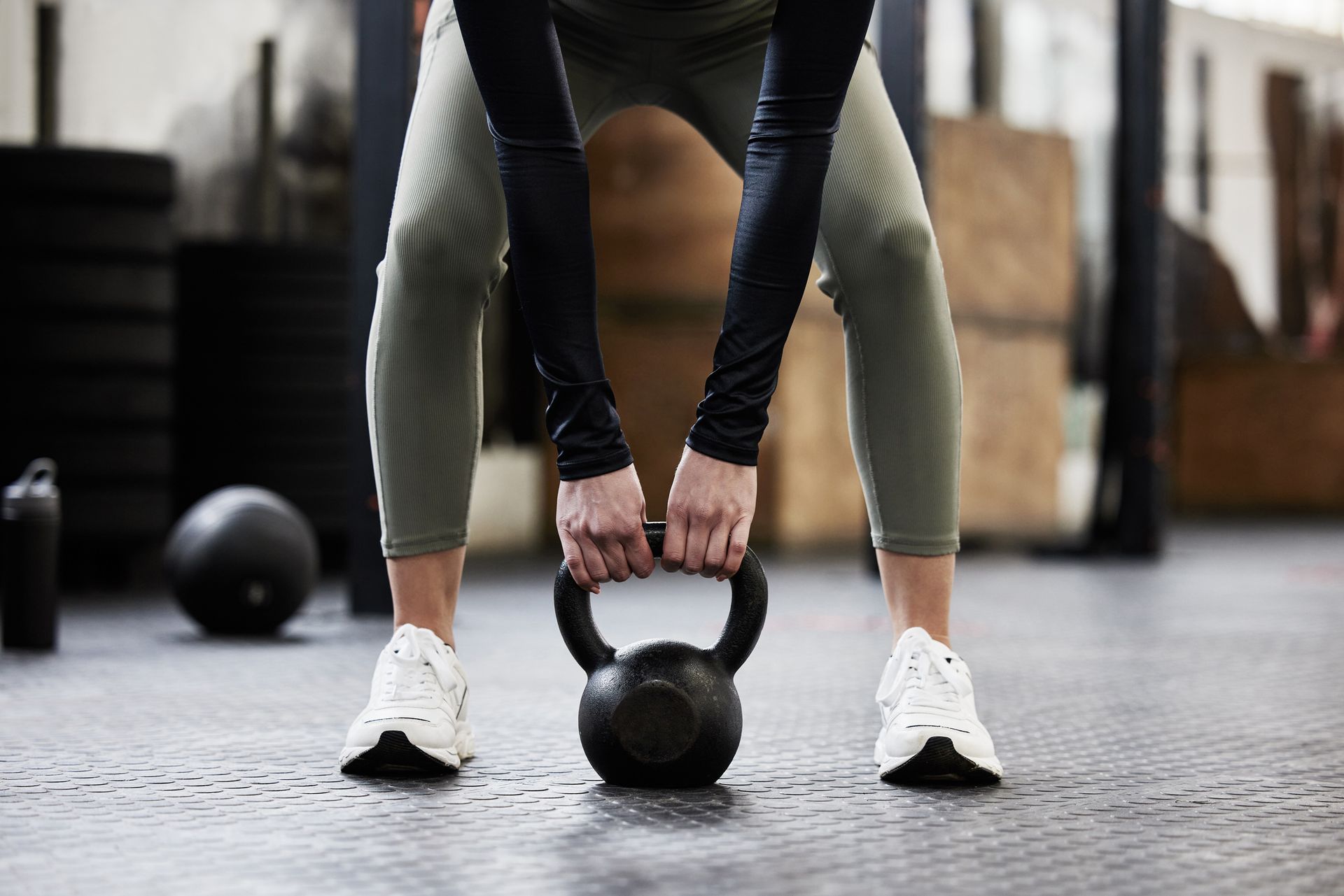 Person in athletic wear gripping a kettlebell on a gym floor.