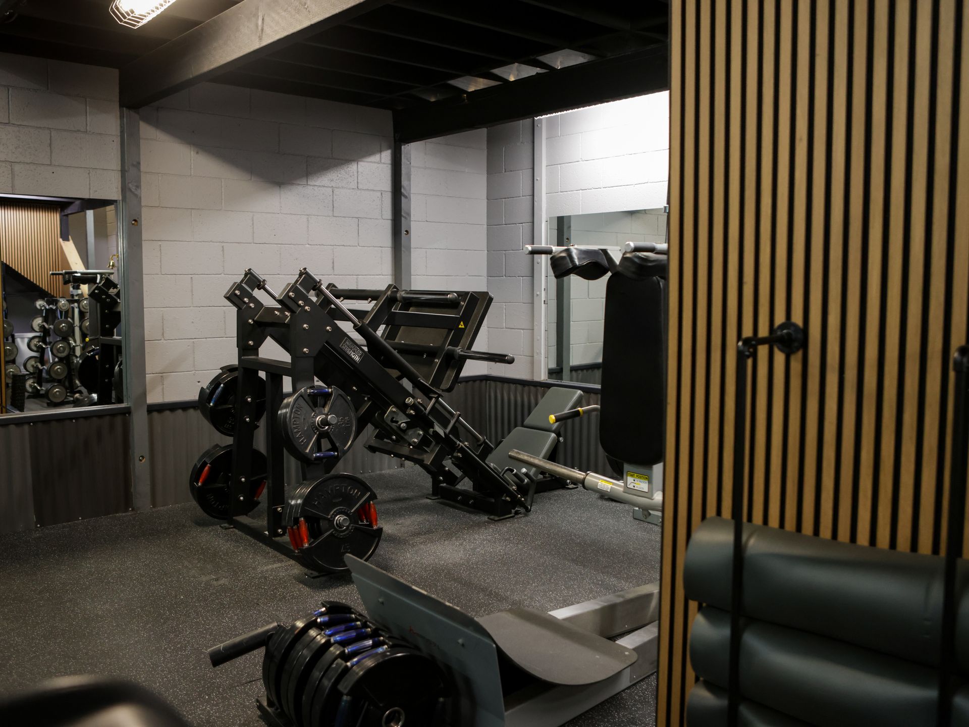 Gym interior with a leg press machine, weights, and wood-paneled wall. Gym interior with a leg press machine, weights, and wood-paneled wall.