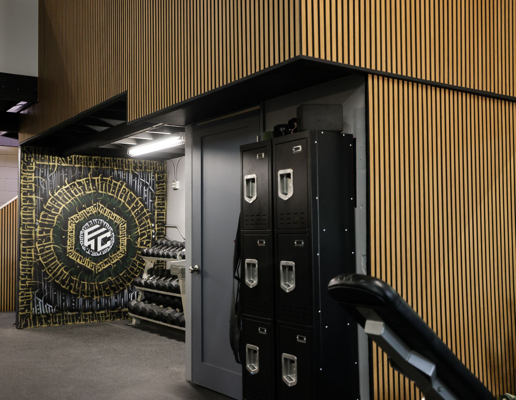 Gym entrance with lockers, weights, and decorative wall art. Wooden paneling. Gym entrance with lockers, weights, and decorative wall art. Wooden paneling.