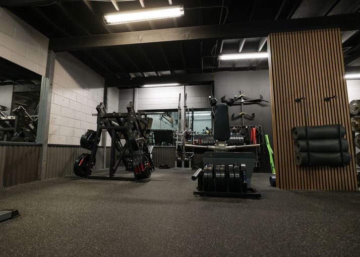 Woman in a black sports bra looks away in a gym, with weights on a rack in the background. Woman in a black sports bra looks away in a gym, with weights on a rack in the background.