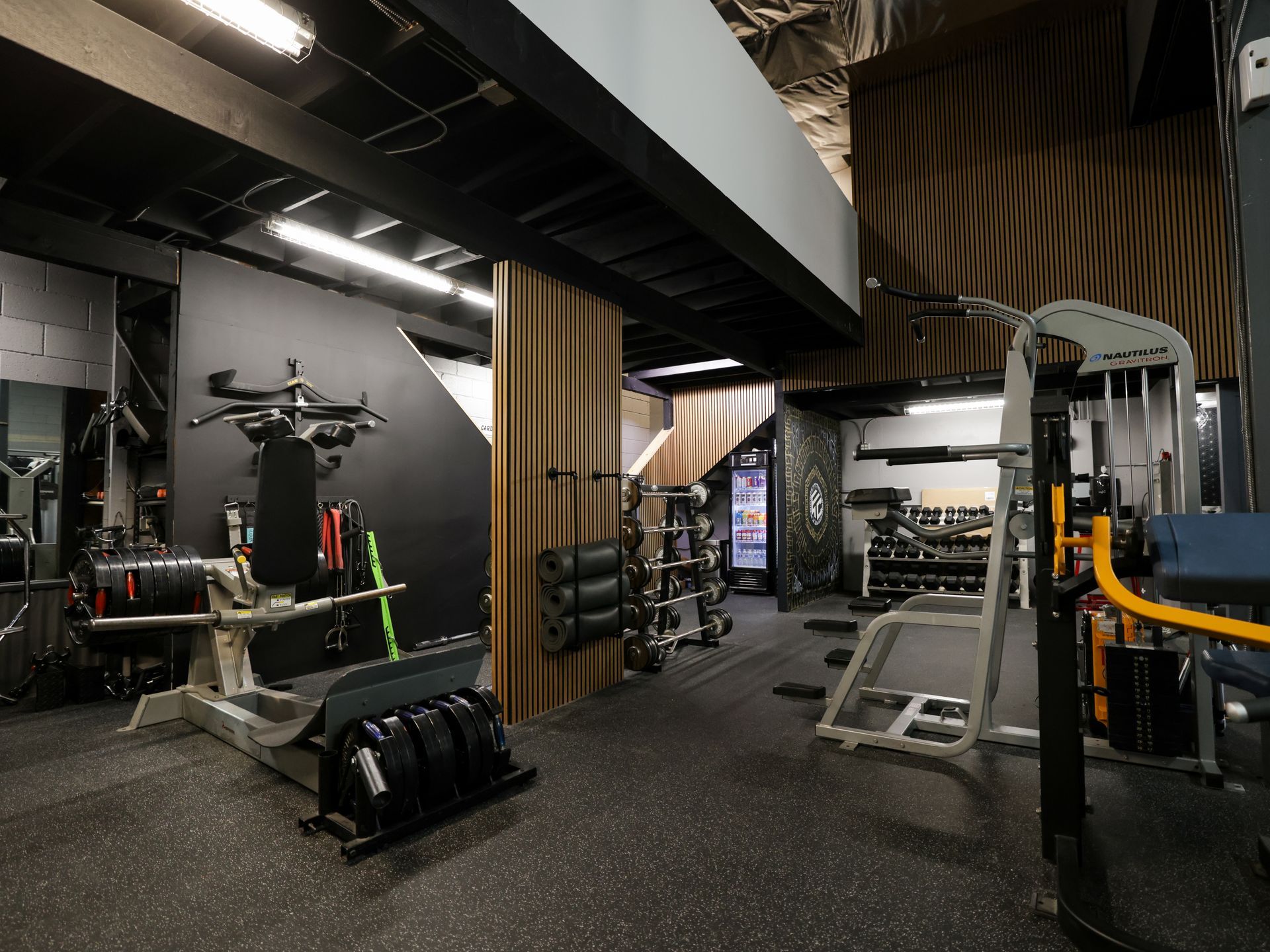 Two women smiling, lifting dumbbells in a gym. They are wearing workout clothes.