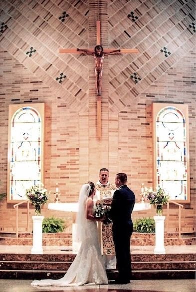 A bride and groom are getting married in a church under a cross.