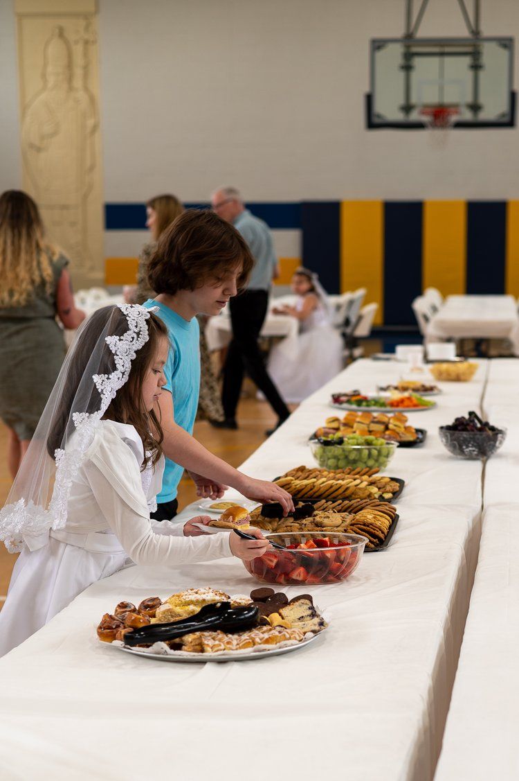 A girl in a communion dress is standing at a long table with plates of food.