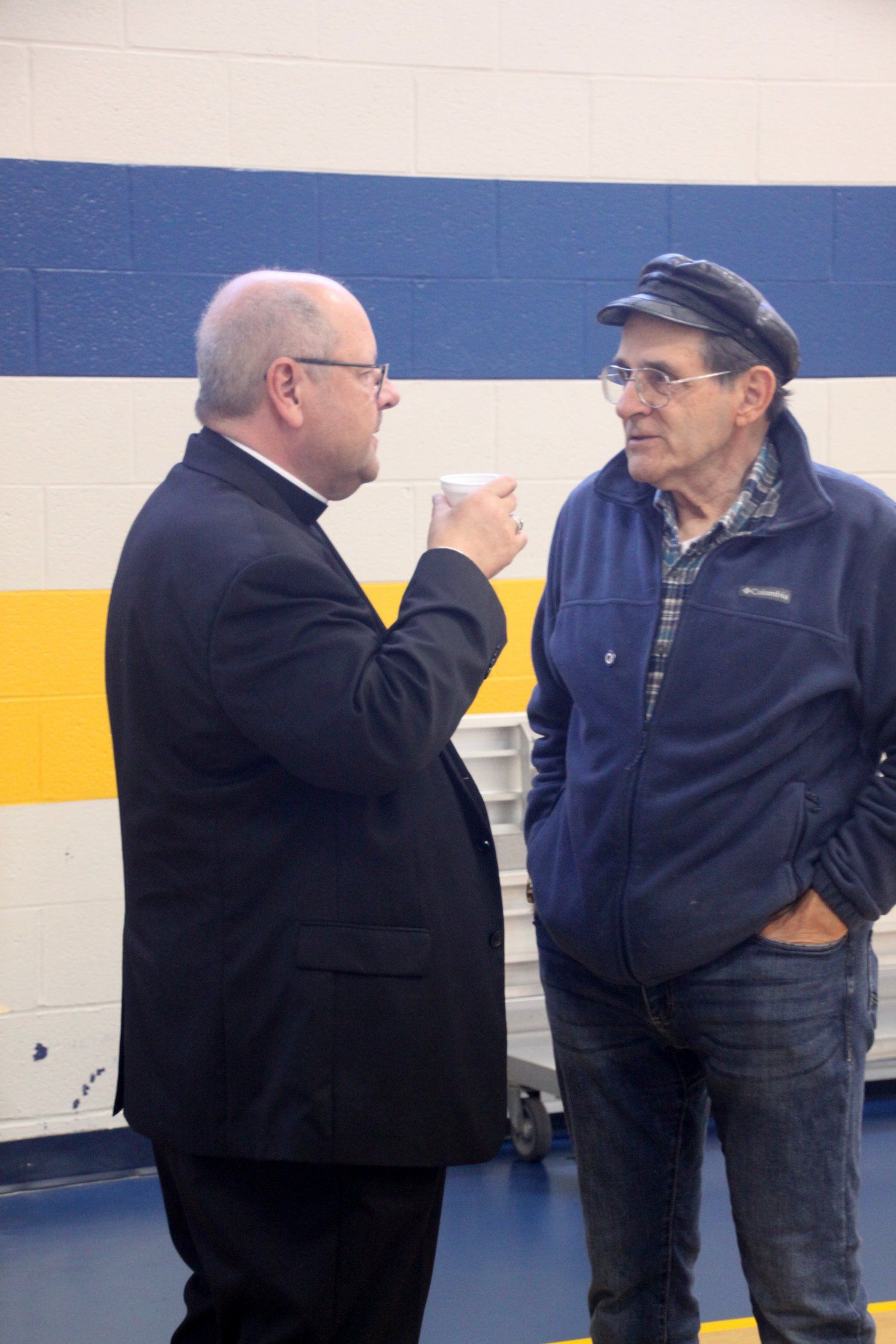 Two men are talking in front of a blue and white wall