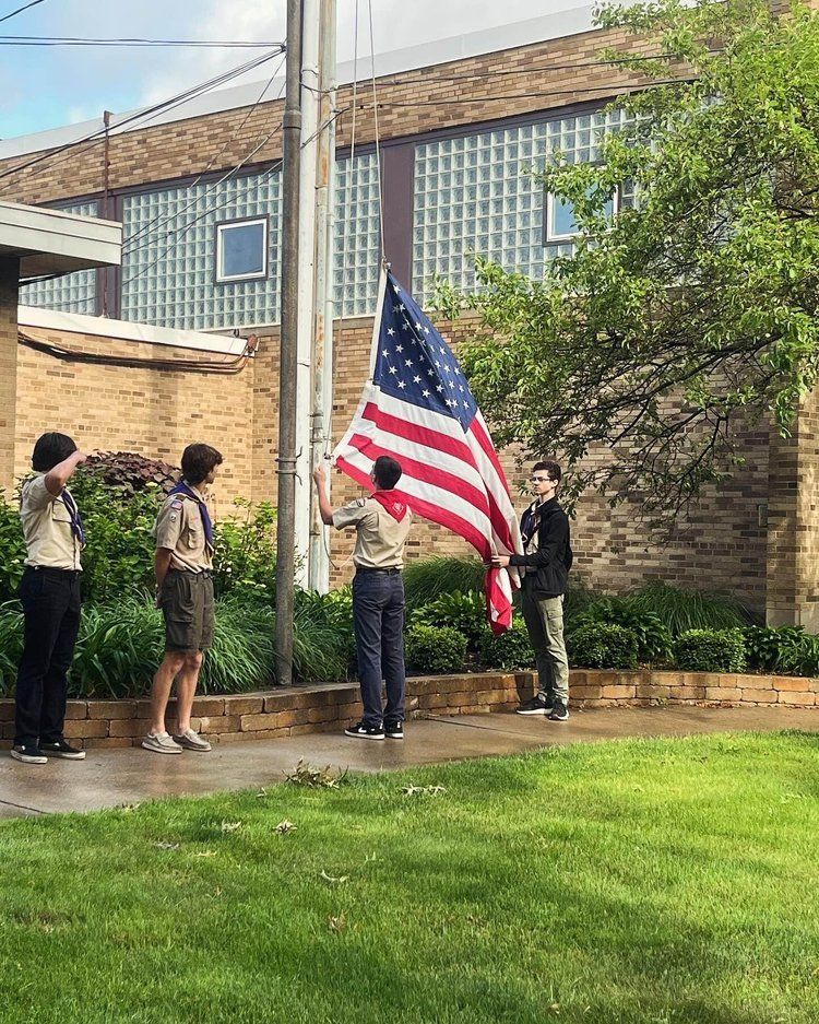 A group of boy scouts are raising an american flag in front of a building.