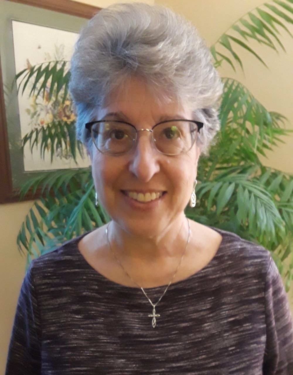 A woman wearing glasses and a cross necklace smiles for the camera