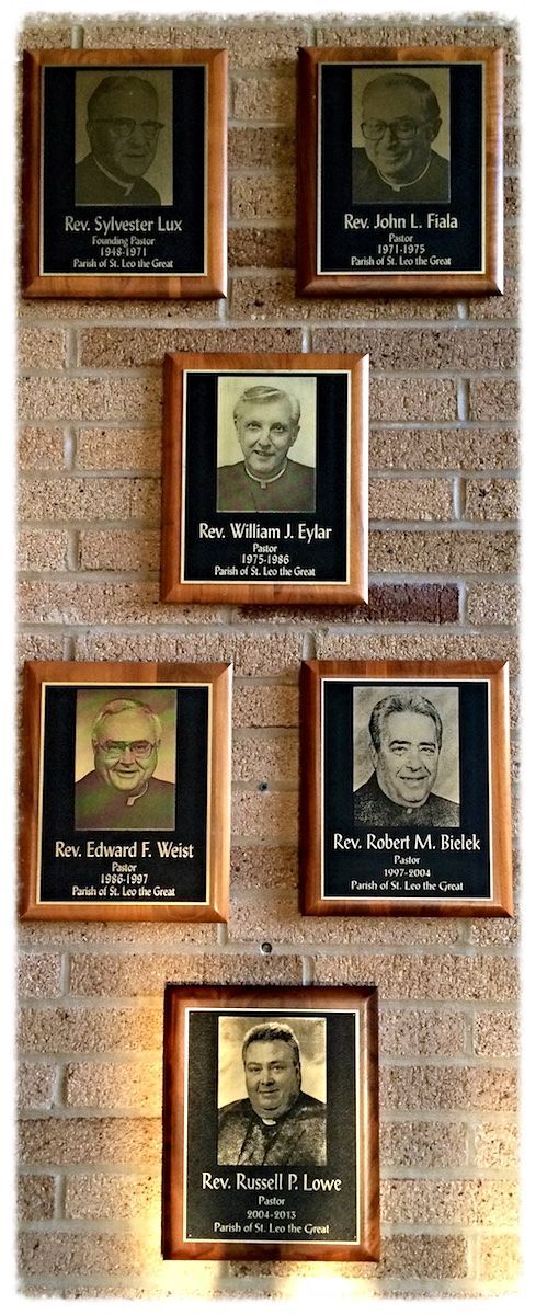 A row of framed pictures of previous pastors on a brick wall.