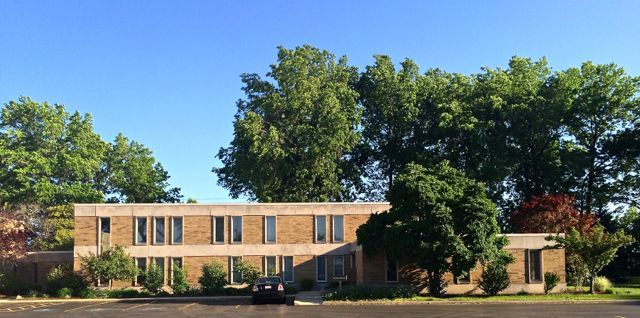 A large brick building with trees in front of it and a car parked in front of it.