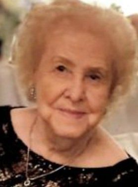 A close up of an elderly woman wearing a black dress and a necklace.