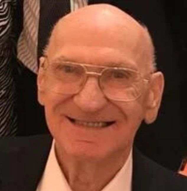 A bald man wearing glasses and a suit is smiling for the camera.