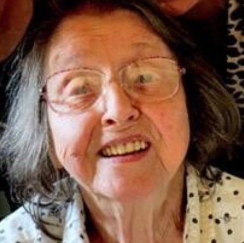 A close up of an elderly woman wearing glasses and smiling.