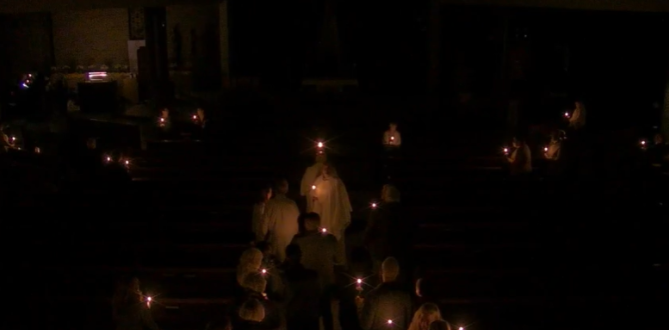 A group of people are holding candles in the dark.