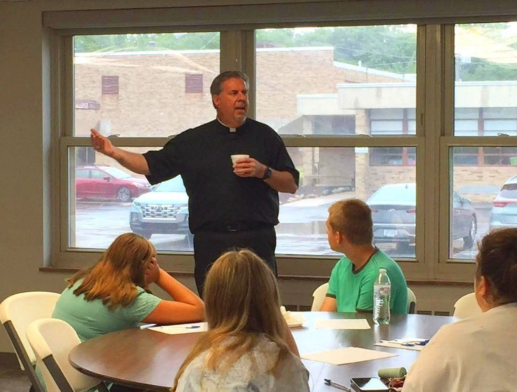the priest is speaking to a group of children in a classroom